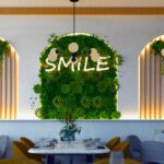 Thumbnail of http://Modern%20Greenleaf%20Cafe%20in%20Notting%20Hill%20interior%20wall%20feature%20with%20“Smile”%20neon%20sign%20and%20green%20foliage.