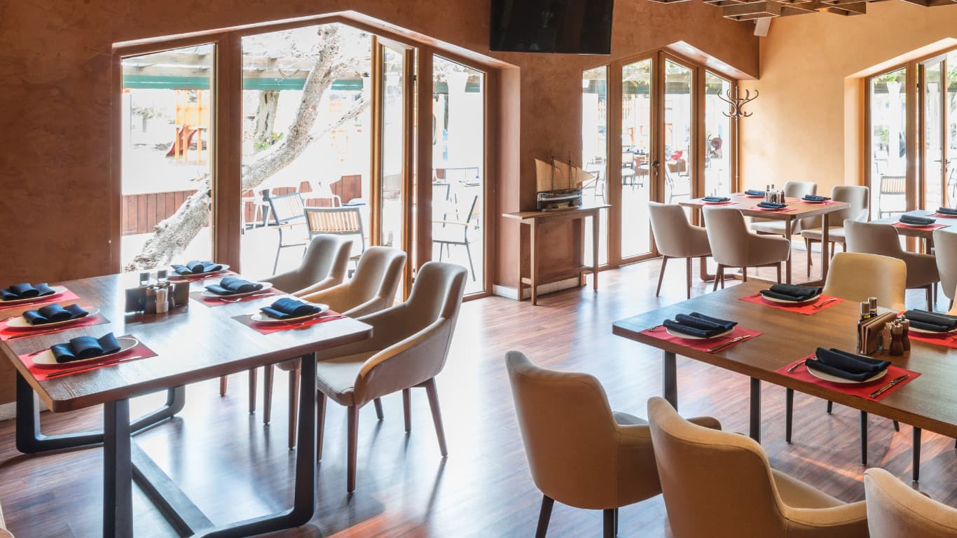 Modern restaurant interior with rustic design featuring natural wood tables and chairs, warm golden walls, large windows, soft lighting fixtures, comfortable booth and table seating, earthy neutral tones, and cosy atmosphere in Dulwich