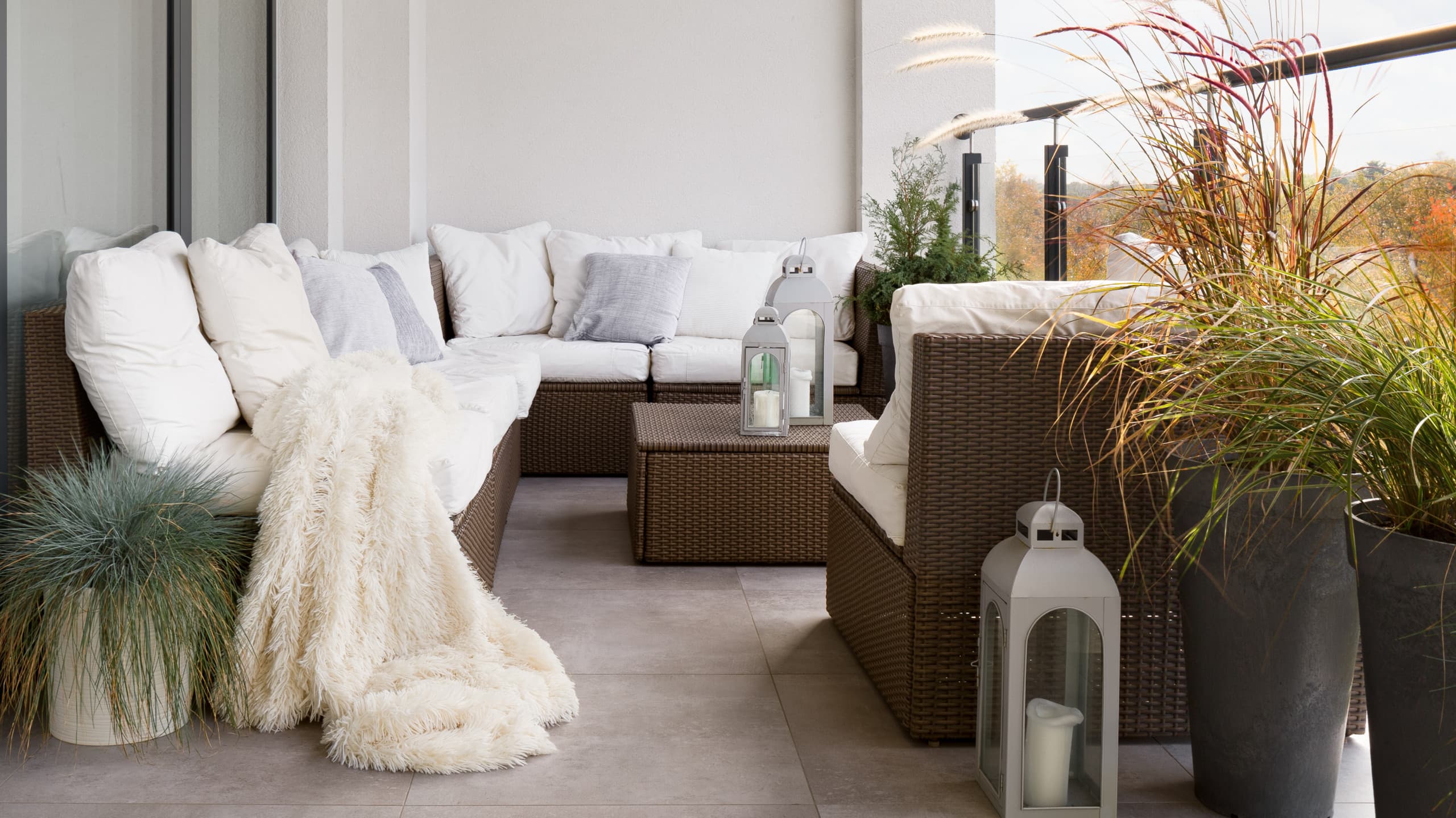 Chic boho balcony in Caterham with rattan corner sofa, soft textiles, and potted grasses.