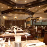 Thumbnail of http://Elegant%20restaurant%20interior%20with%20exposed%20dark%20wood%20beam%20ceiling,%20natural%20travertine%20stone%20accent%20walls,%20white%20tablecloths%20on%20dark%20wood%20tables,%20brown%20leather%20upholstered%20chairs,%20warm%20ambient%20lighting,%20and%20contemporary%20design%20in%20Bexleyheath