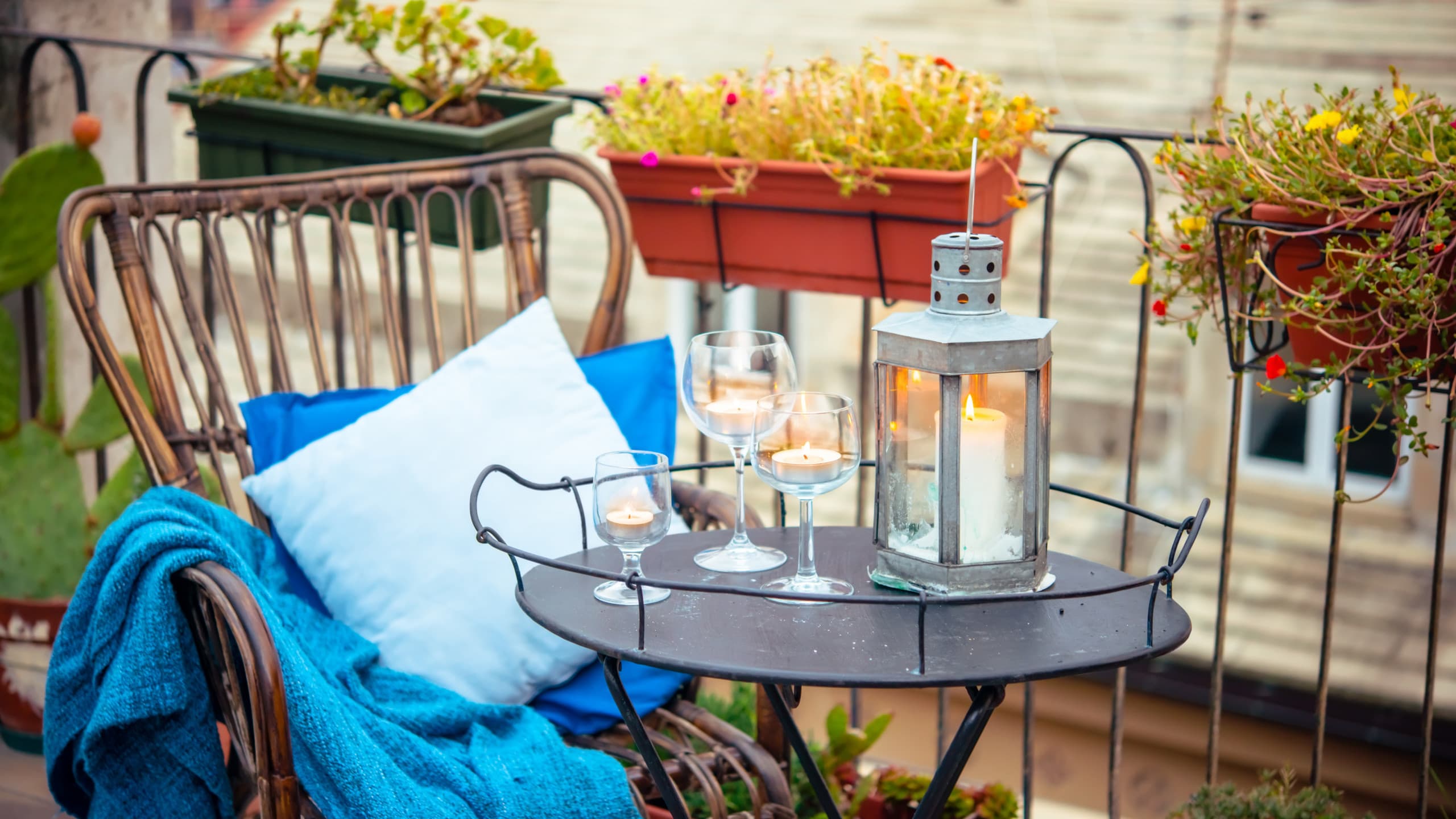 Cosy boho balcony setup with rattan chair, blue textiles, lantern, and planter rail.