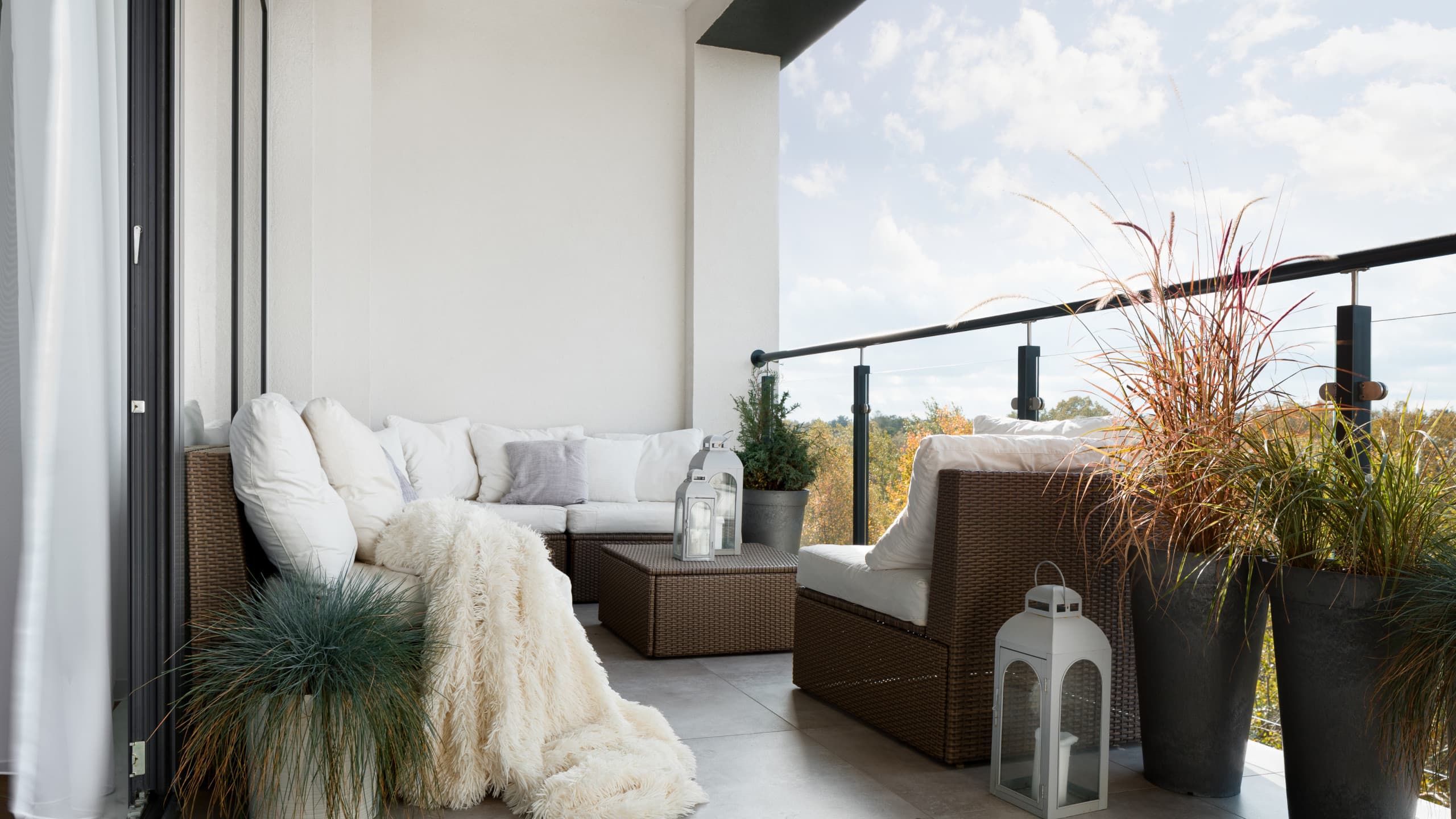 Light-filled boho balcony in Caterham with rattan corner sofa, soft throw, and potted grasses.