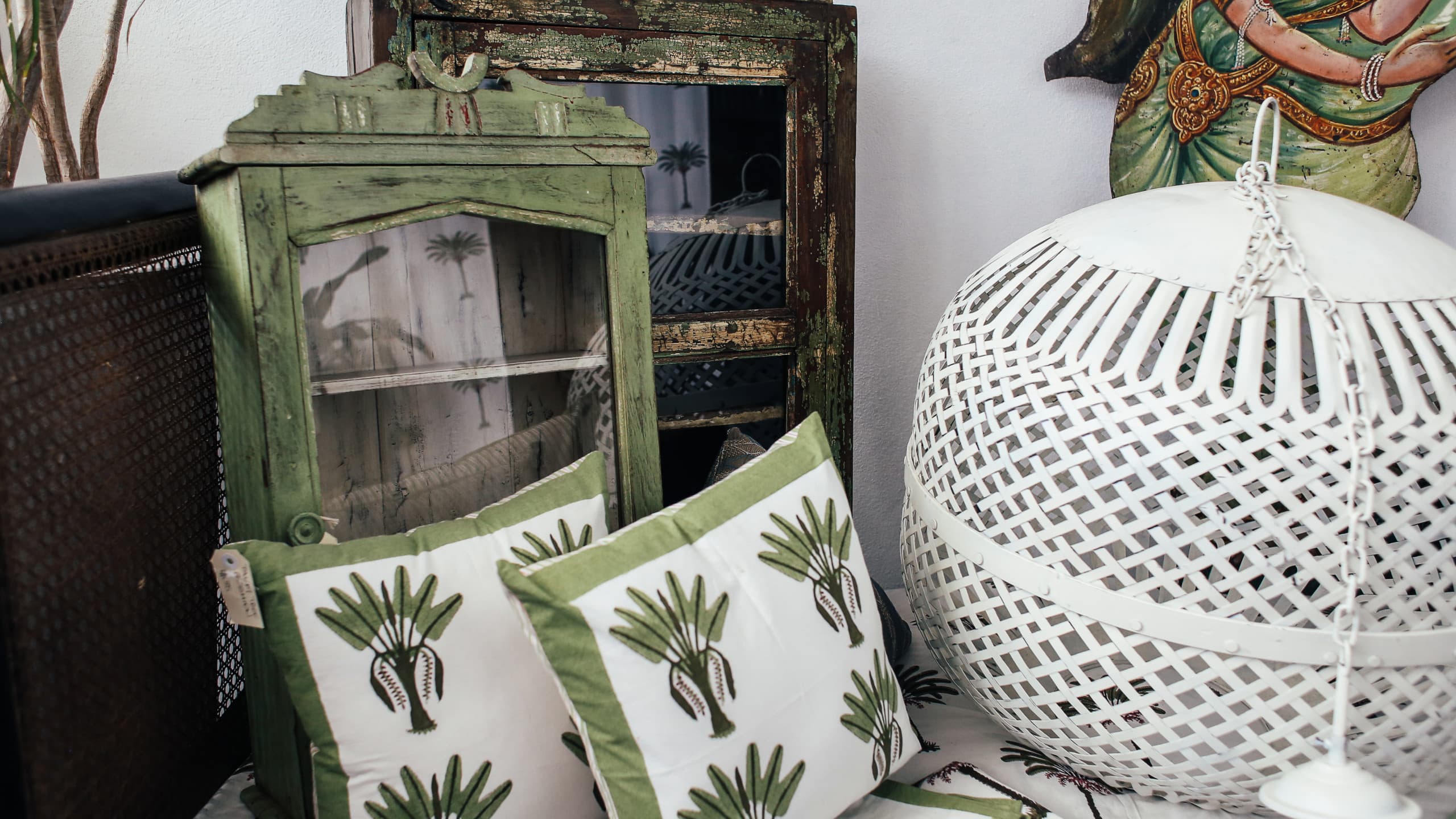 Boho balcony styling vignette with palm-print cushions, rustic cabinets, and white woven lantern.