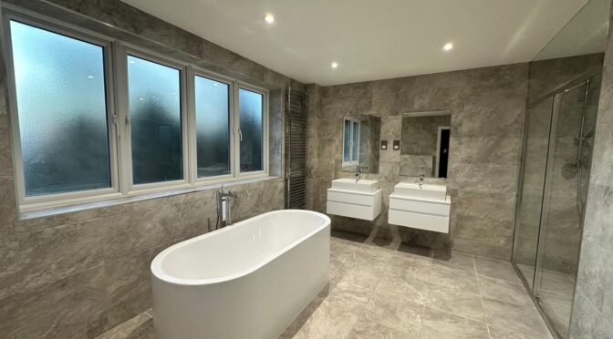 Freestanding bath in modern luxury bathroom with stone-effect tiles and natural light in London