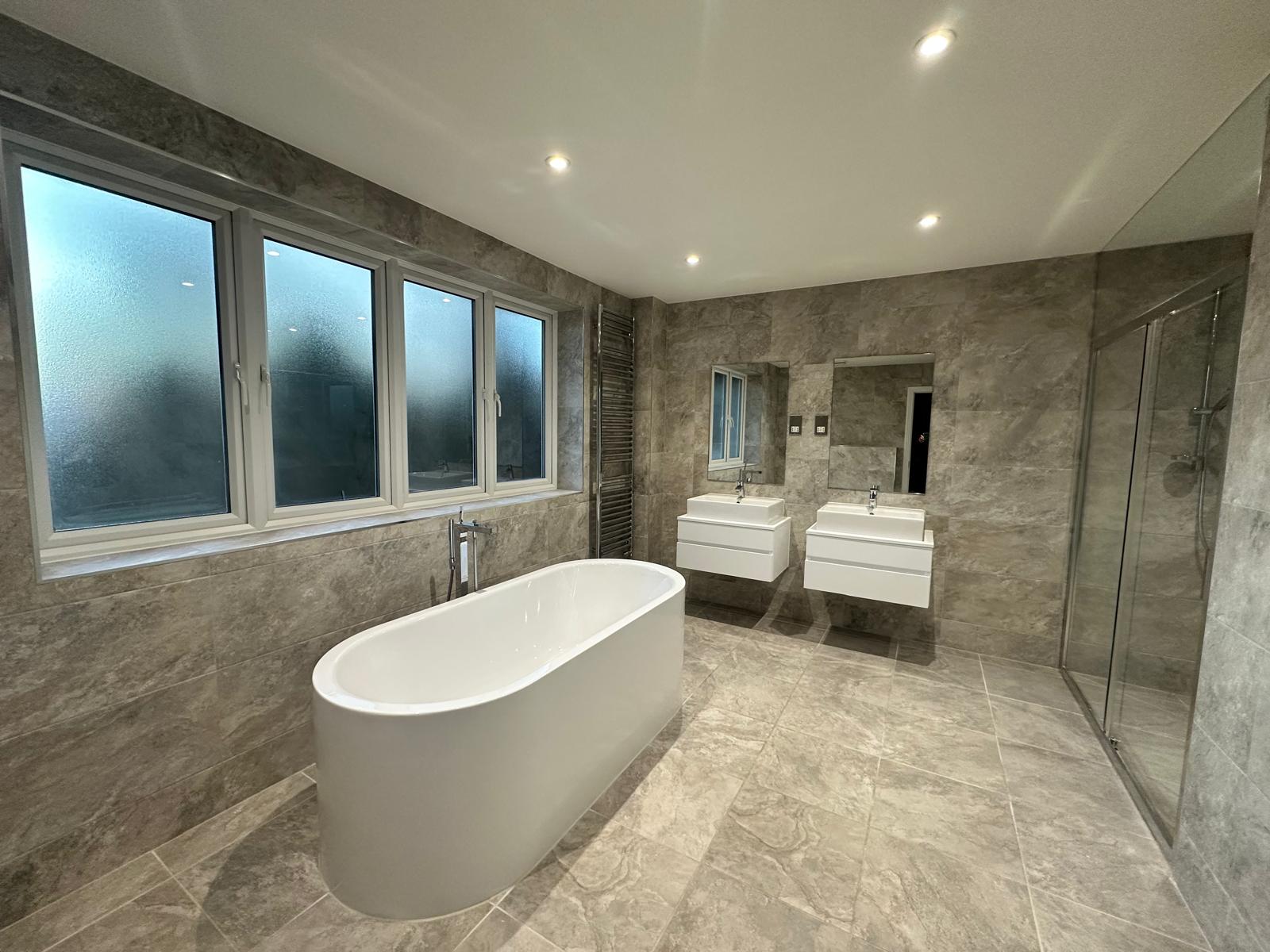 Freestanding bath in modern luxury bathroom with stone-effect tiles and natural light in London