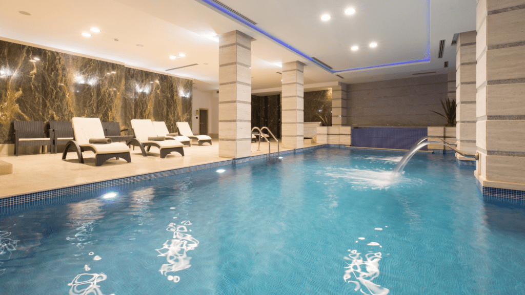 A spa pool space enclosed by marble structures and soothing light design with lounge seating features interior design by a top London firm. 