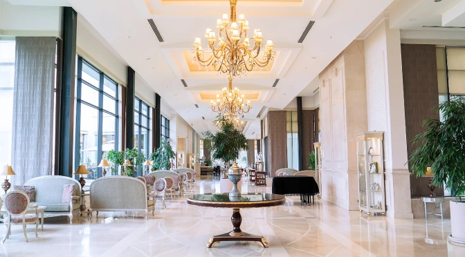 A grand luxury hotel lobby in London designed by Oraanj Interior Design, featuring chandeliers, plush seating, marble flooring, and elegant décor that creates a welcoming and sophisticated ambiance.